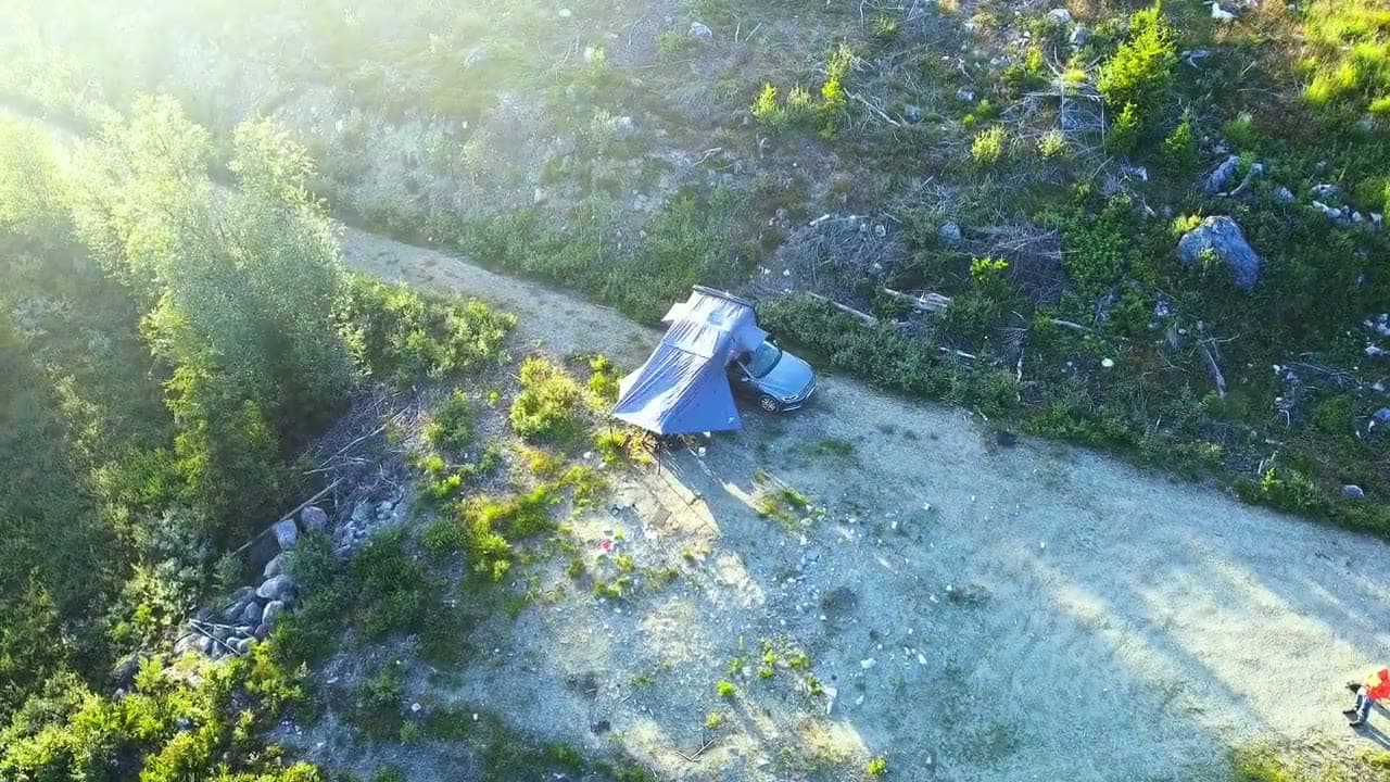 Dronefoto af tagteltet på en bil med markisen slået ud på en grusvej